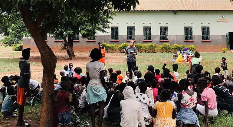 En grupp människor sitter under ett träd i Zambia.
